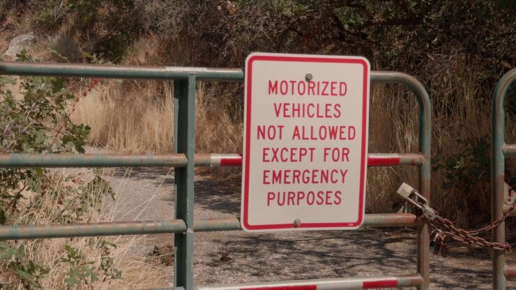 Still shot of a posted vehicle restriction sign attached to a metal trail gate.