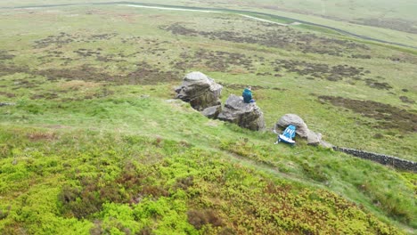 A-phenomenal-aerial-shot-over-a-solo-traveller-sitting-on-the-edge-of-the-rocky-hill