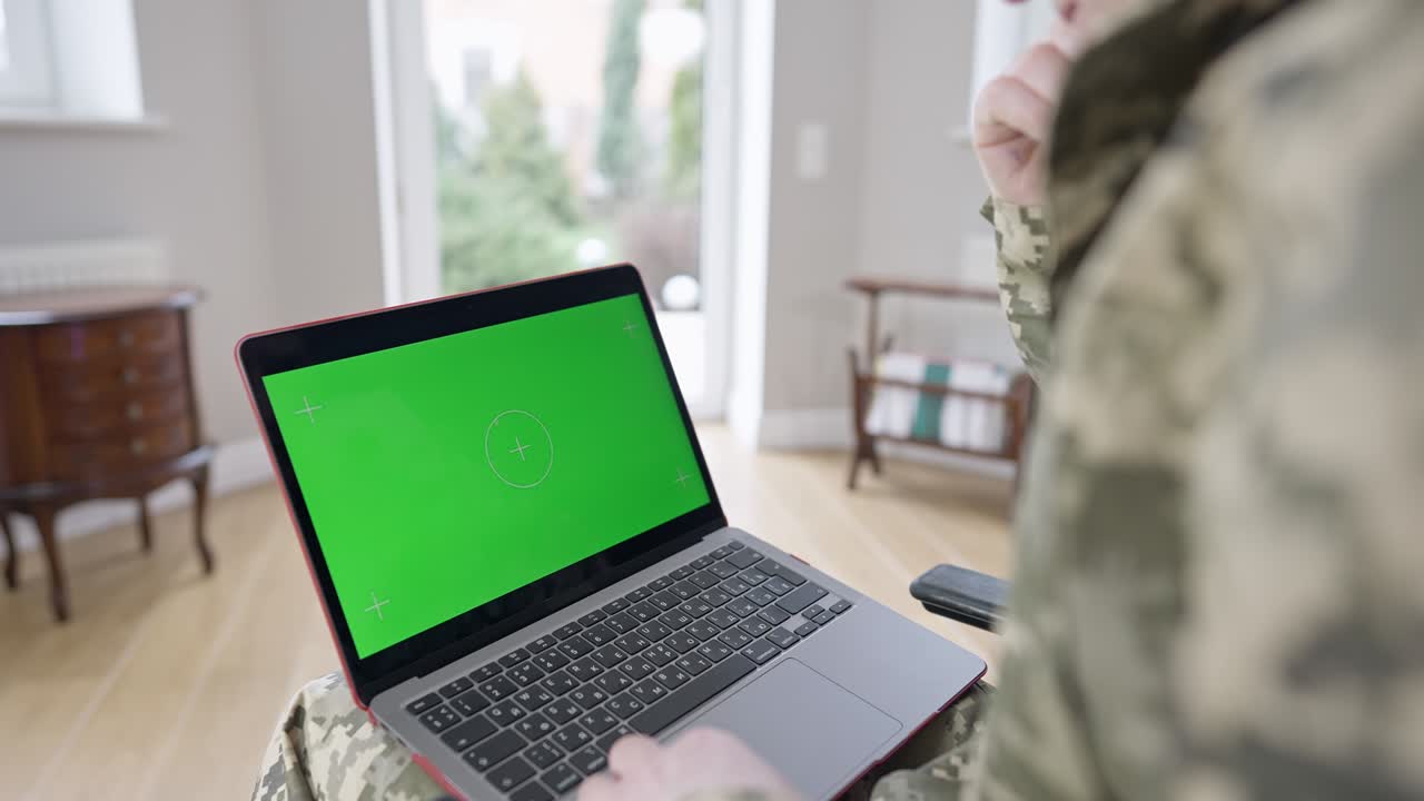 portátil con pantalla verde en las rodillas de hombre militar caucásico irreconocible en el interior. soldado adulto o veterano navegando por internet o mensajería en línea en el hogar. tecnologías modernas, chromakey.