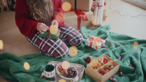 woman tying red ribbon on wrapped christmas gift at home