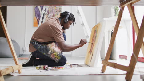african american male artist wearing headphones painting on canvas at art studio