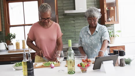 Amigas-Afroamericanas-Mayores-Cocinando,-Cortando-Verduras-Y-Usando-Tabletas,-Cámara-Lenta