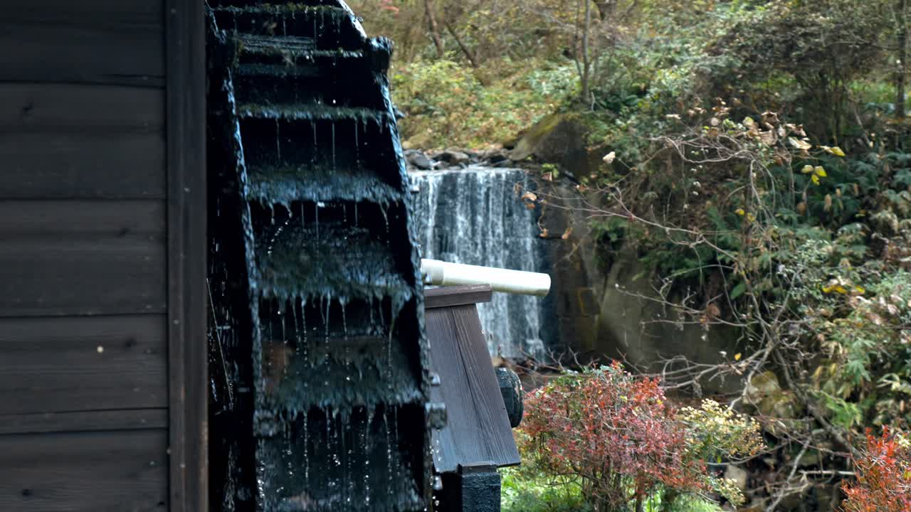 A stunning shot of a traditional Japanese water mill situated along the Nakasendo Trail, with a picturesque waterfall flowing in the background.