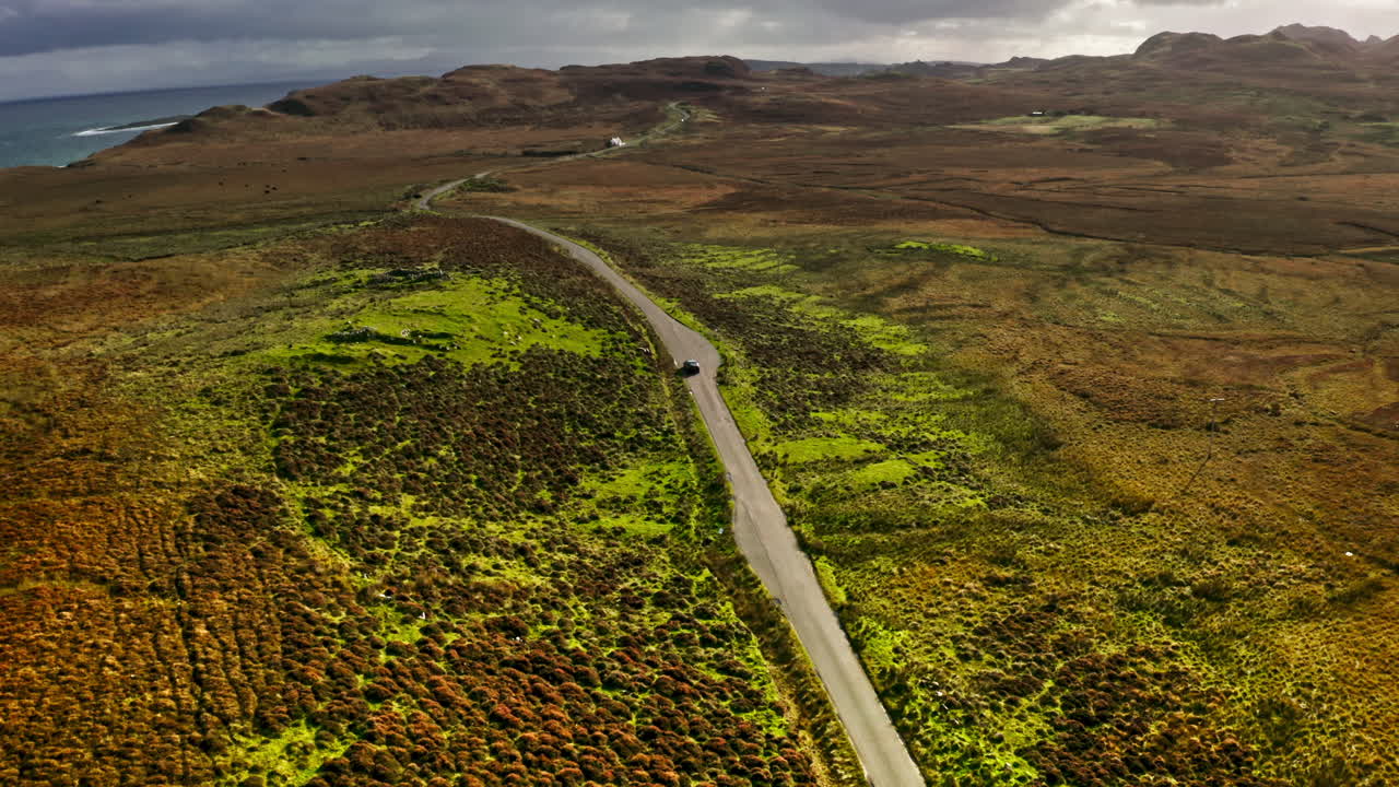 Car Driving On Winding Road Through Rugged Moorland On Isle Of Skye In Scotland, UK. aerial tilt-up shot