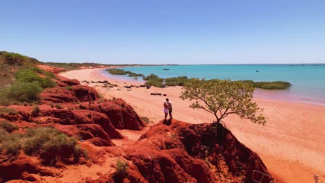 couple on red cliffs overlooking turquoise beach