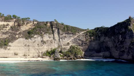 sandy diamond beach in nusa penida island indonesia with rock walls behind, aerial dolly out reveal shot