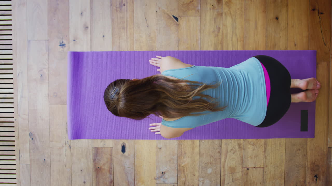 vista aérea de una mujer joven haciendo yoga en el suelo de madera