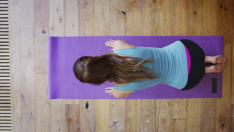 Vista-Aérea-De-Una-Mujer-Joven-Haciendo-Yoga-En-Un-Piso-De-Madera