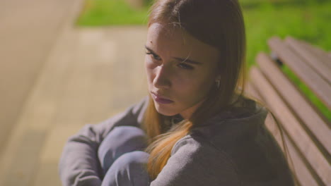 close-up of a tired young woman sitting on a bench outdoors at night, looking sleepy and contemplative, surrounded by soft blurred background