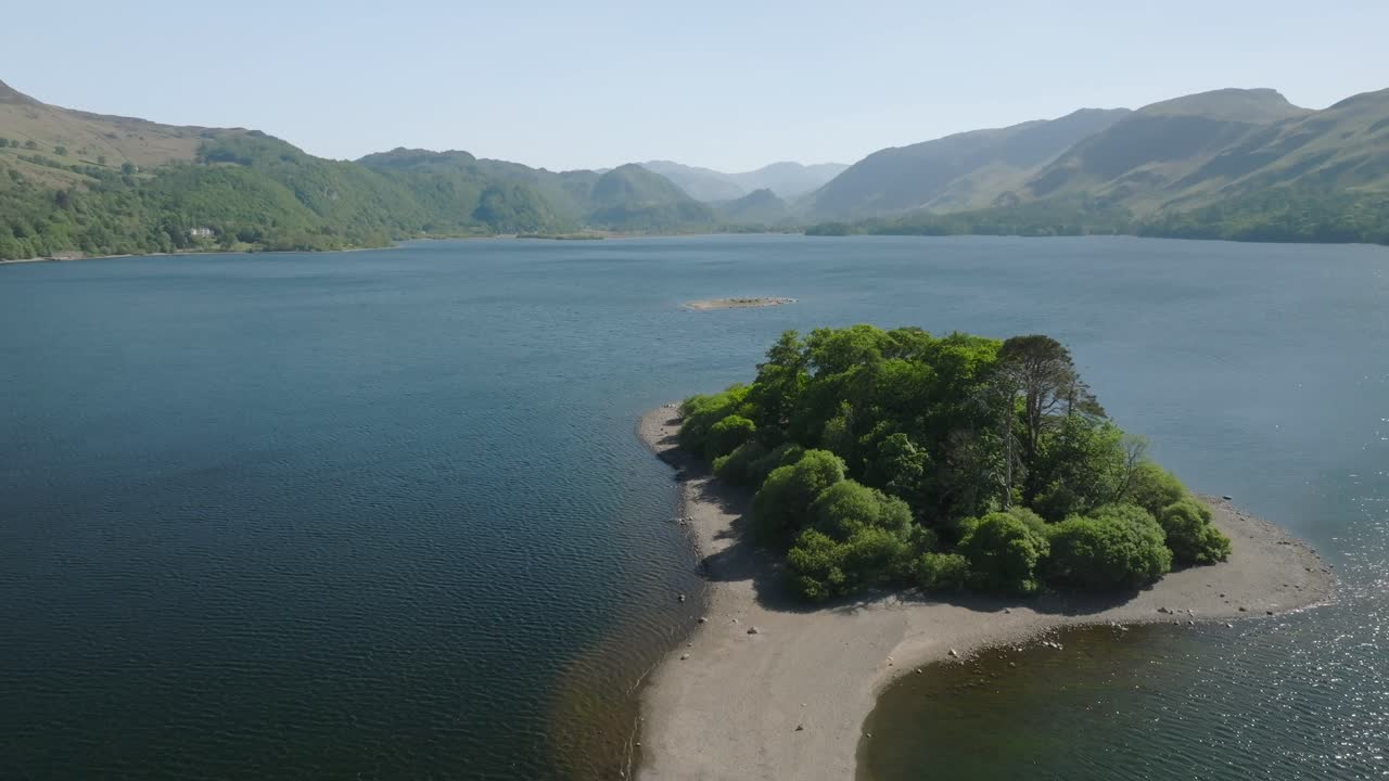 Flying towards small island in Cumbrian lake with mountains in the distance. Derwentwater, Lake District, Cumbria, UK.