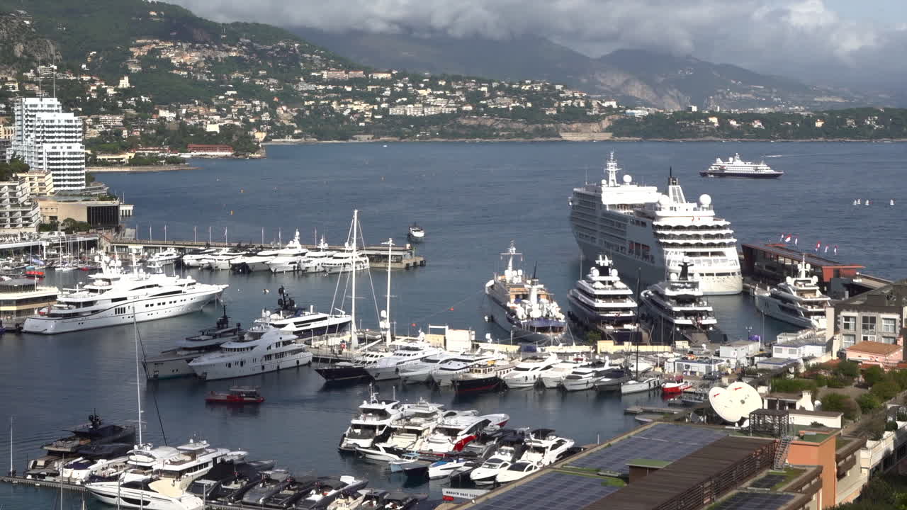 View over Monaco's marina packed with yachts, a large cruise ship docked at the terminal with Cap-Martin and coastal hills beyond
