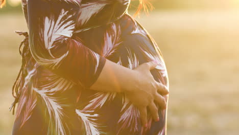 pregnant woman rubs her belly during a peaceful evening sunset