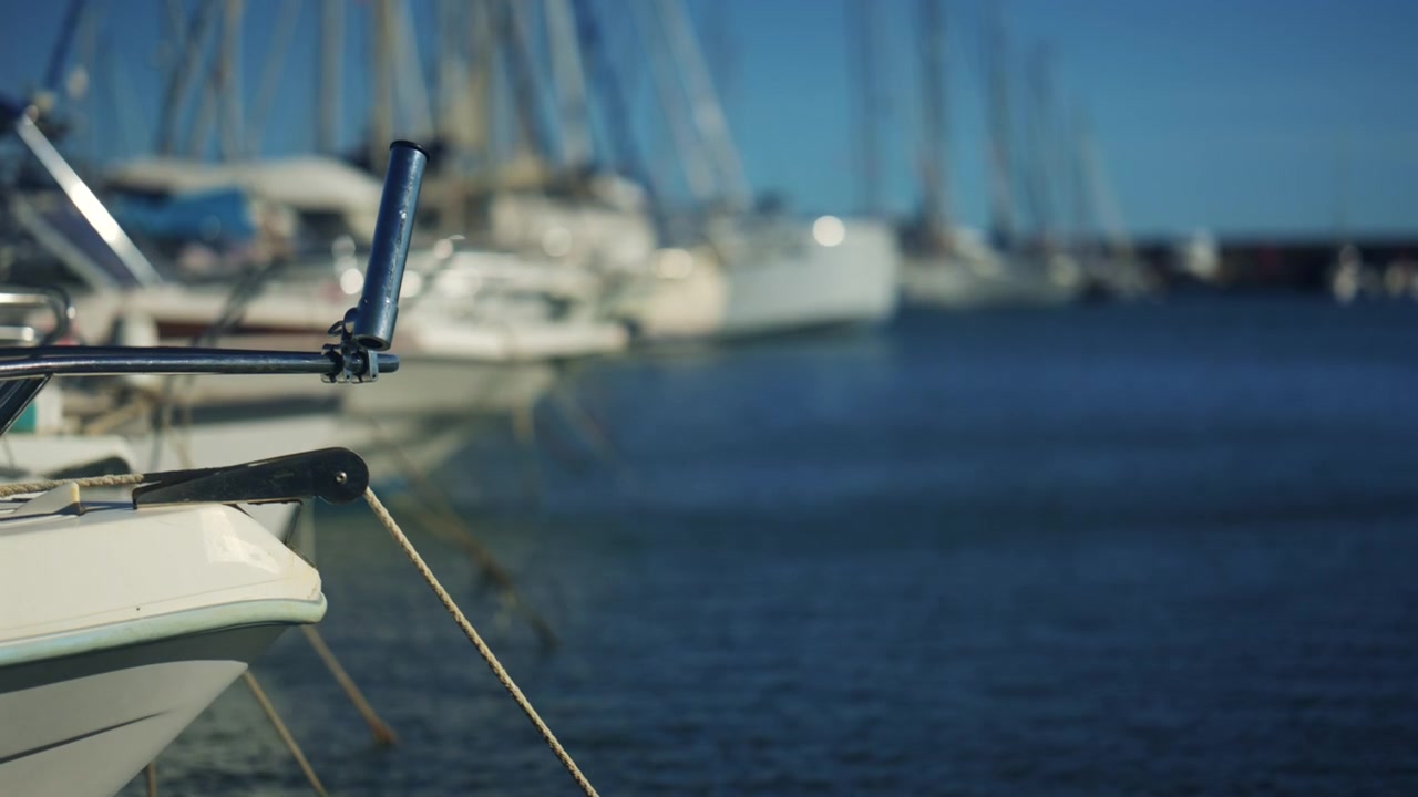 Close up of a metal boat rod holder and mooring rope, with soft focus sailboats and marina water creating a nautical summer scene
