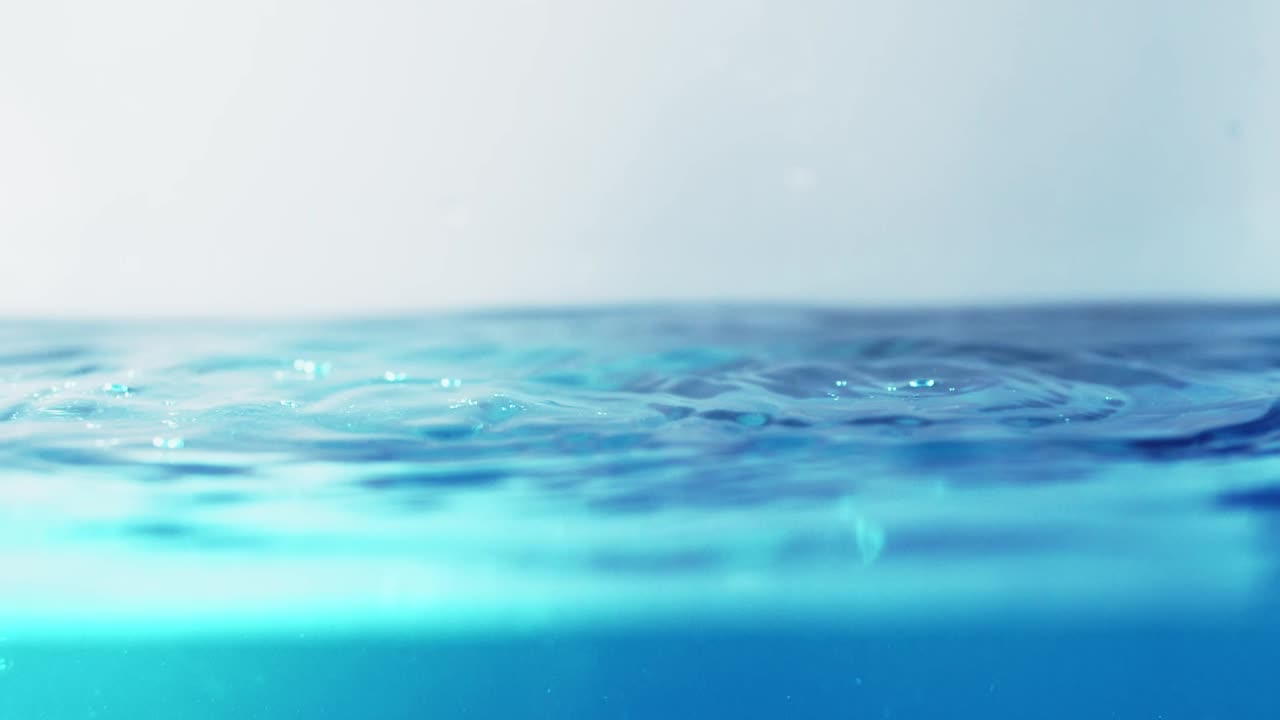 슬로우 모션의 깨끗한 물 표면은 물이 튀는 상점으로 화면을 채우고 기포로 액체 표면을 흔들고 있습니다.