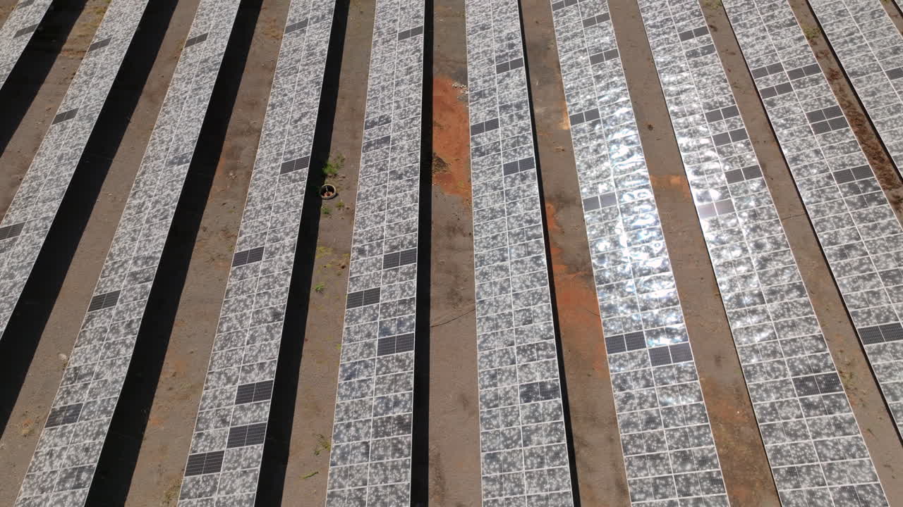 Solar farm rows reveal widespread hail damage in a wide aerial overflight, highlighting shattered panel surfaces and renewable infrastructure risk