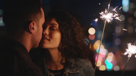 happy caucasian couple kissing on rooftop at night holding sparklers celebrating anniversary enjoying romantic urban evening