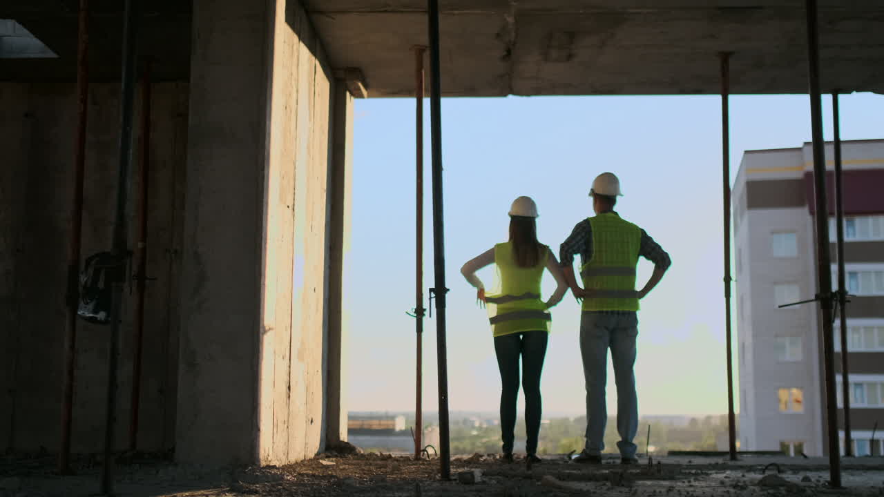 los constructores miran un paisaje urbano en un fondo de puesta de sol vista trasera.