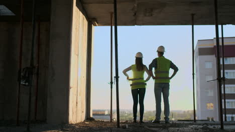 Builders-look-at-a-cityscape-on-a-sunset-background-back-view.