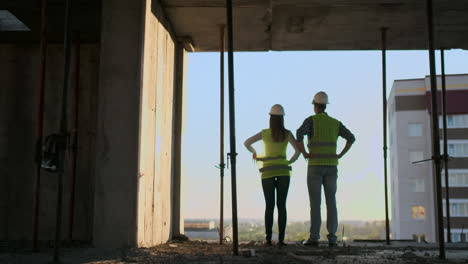 los constructores miran un paisaje urbano en un fondo de puesta de sol vista trasera.