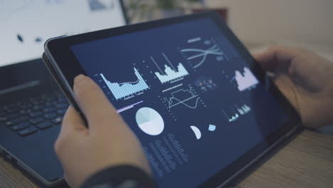 Person-holds-tablet-screen-on-which-various-diagrams,-graphs,-bars,-figures-for-analyzing-stock-market-deal-can-be-seen