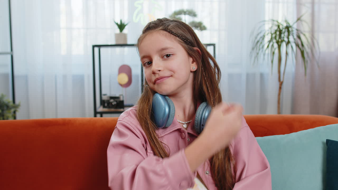Portrait of happy smiling young girl child kid with headphones around neck sitting on home sofa