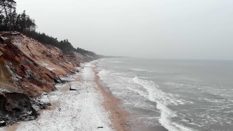 Aerial-shot-of-sandy-beach-in-Ustka-in-winter-with-silhouette-of-a-person-walking