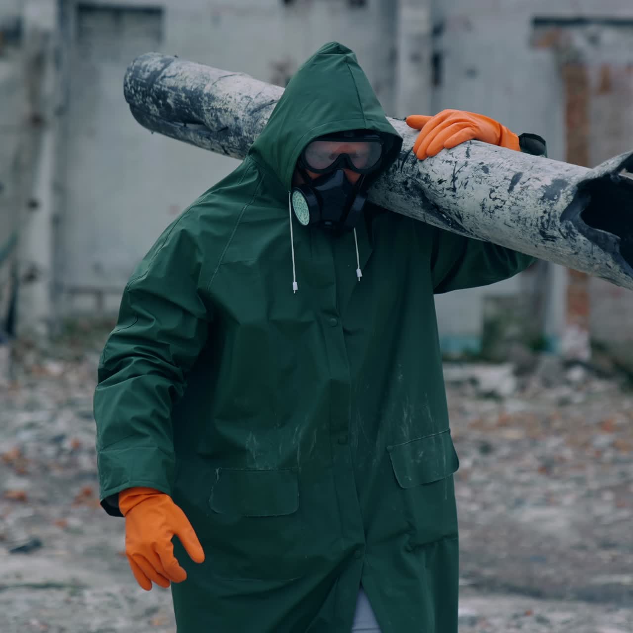 Worker in protective suit in radiation zone. Builder in safety uniform and gas mask is carrying pipe in destroyed place. Chemical attack