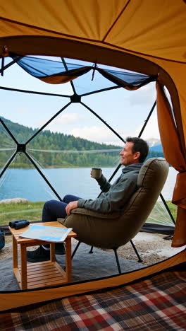 man relaxing in a geodesic dome tent by a scenic mountain lake