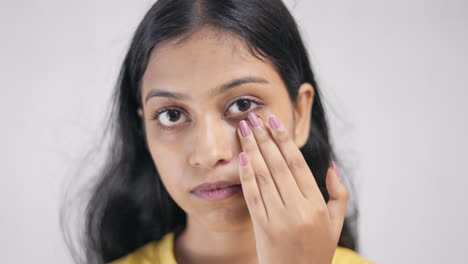 close up portrait of a young lady applying nourishing cream on her under eye area in white background.