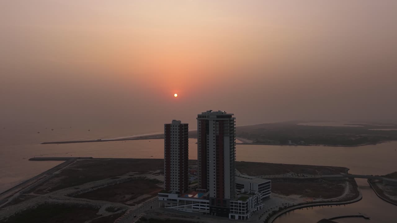 Cinematic aerial drone footage of a modern skyscraper in Eko Atlantic City, Lagos, at sunset, with a calm river beside the building and warm golden hour light