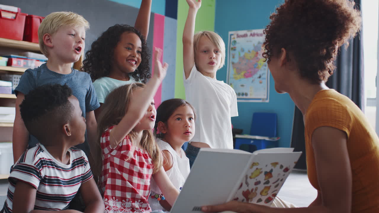 alumnos de primaria levantando las manos para responder a una pregunta mientras la maestra lee una historia en el aula