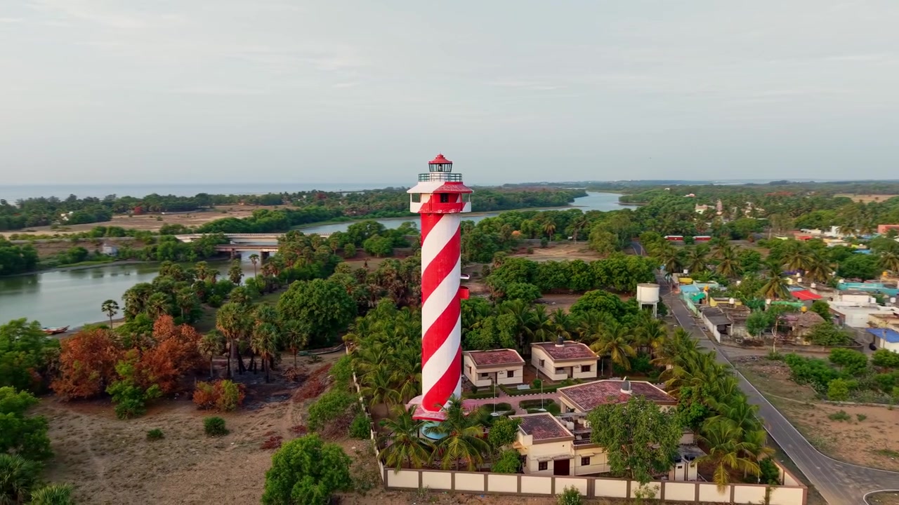 Ripresa aerea con drone di un faro a strisce rosse e bianche circondato da palme, un villaggio e un paesaggio costiero vicino a Chennai nel Tamil Nadu, India, durante il giorno.