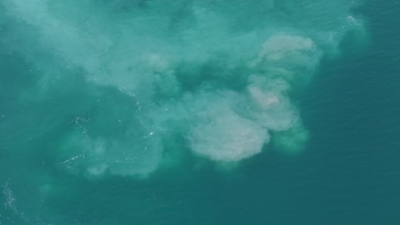 Aerial drone view of turquoise coastal waters with visible underwater sand formations and swirling currents