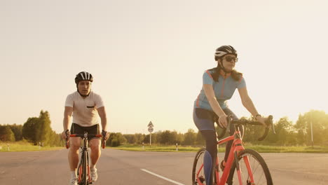 steadicam shot of two healthy mem and woman peddling fast with cycling road bicycle at sunset