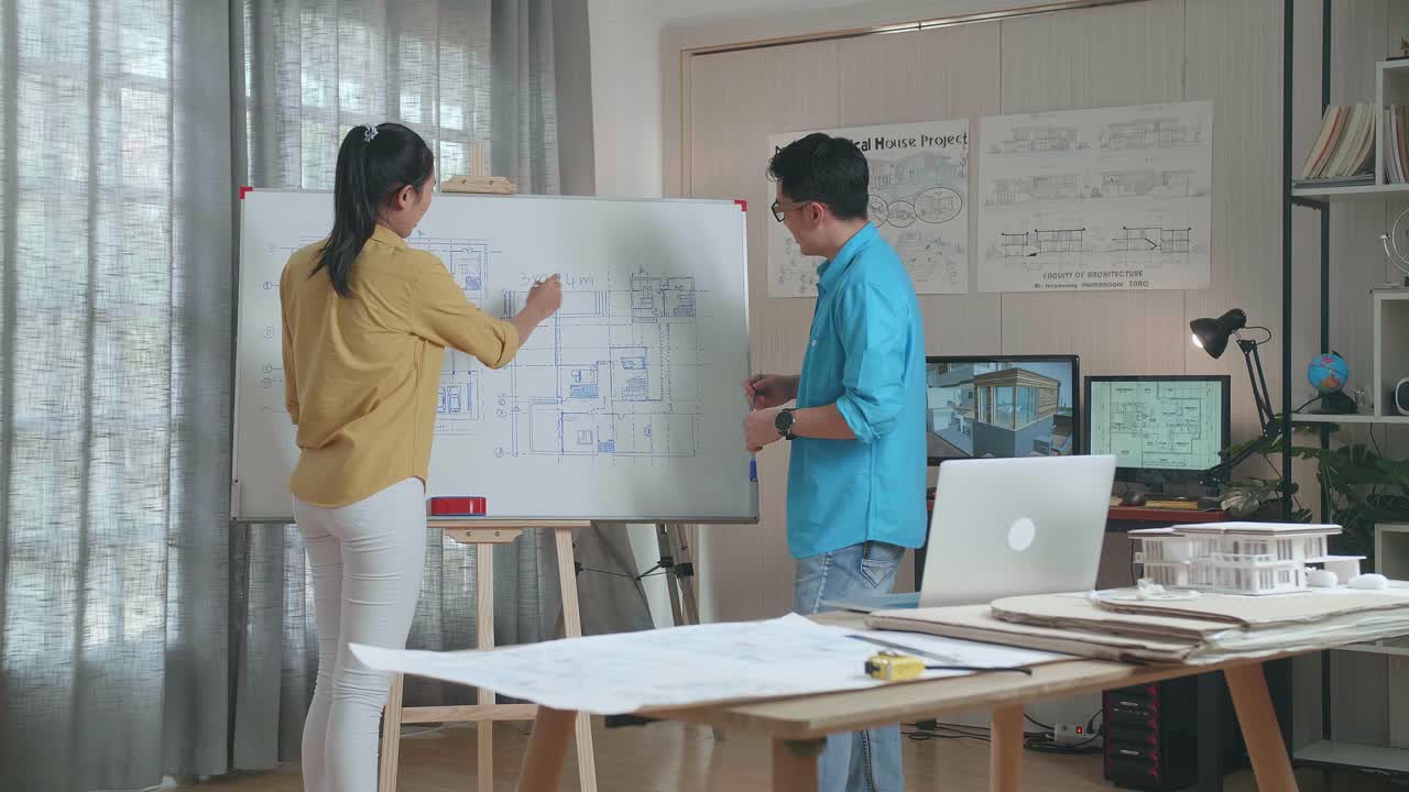 Asian Woman And Man Engineers With Blueprint On Whiteboard Discuss About Design At The Office