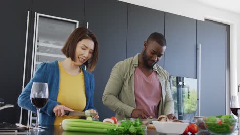 video of happy diverse couple preparing food and smiling at each other in kitchen at home