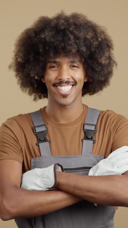 a smiling man with an afro and mustache wearing overalls and gloves