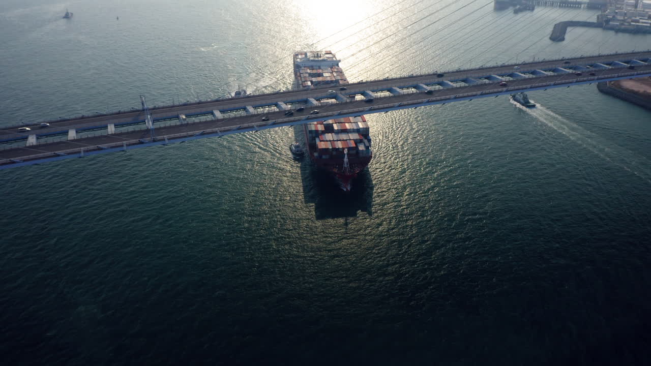 홍콩의 스톤커터 다리를 통과하는 동안 예인선이 바다를 향해 항해하는 예인선의 도움을 받는 거대한 컨테이너선