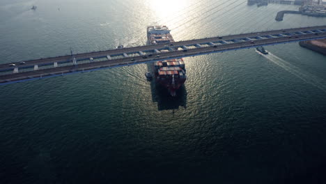 giant container vessel assisted by a tugboat setting sail to open sea while passing the stonecutters bridge in hong kong