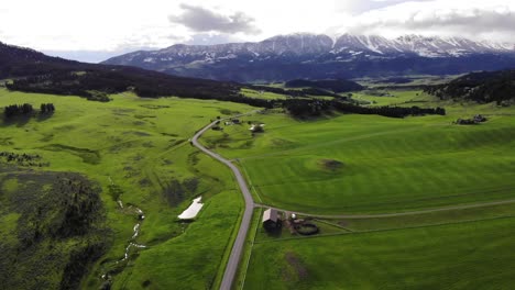 drone shot over a road and green fields with snowy mountains ahead