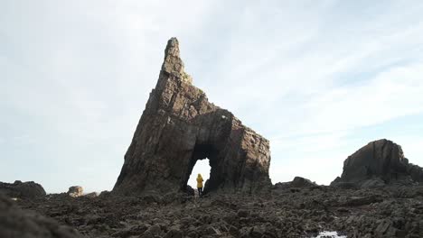 Person-standing-in-arch-of-natural-rocky-formation-on-shore