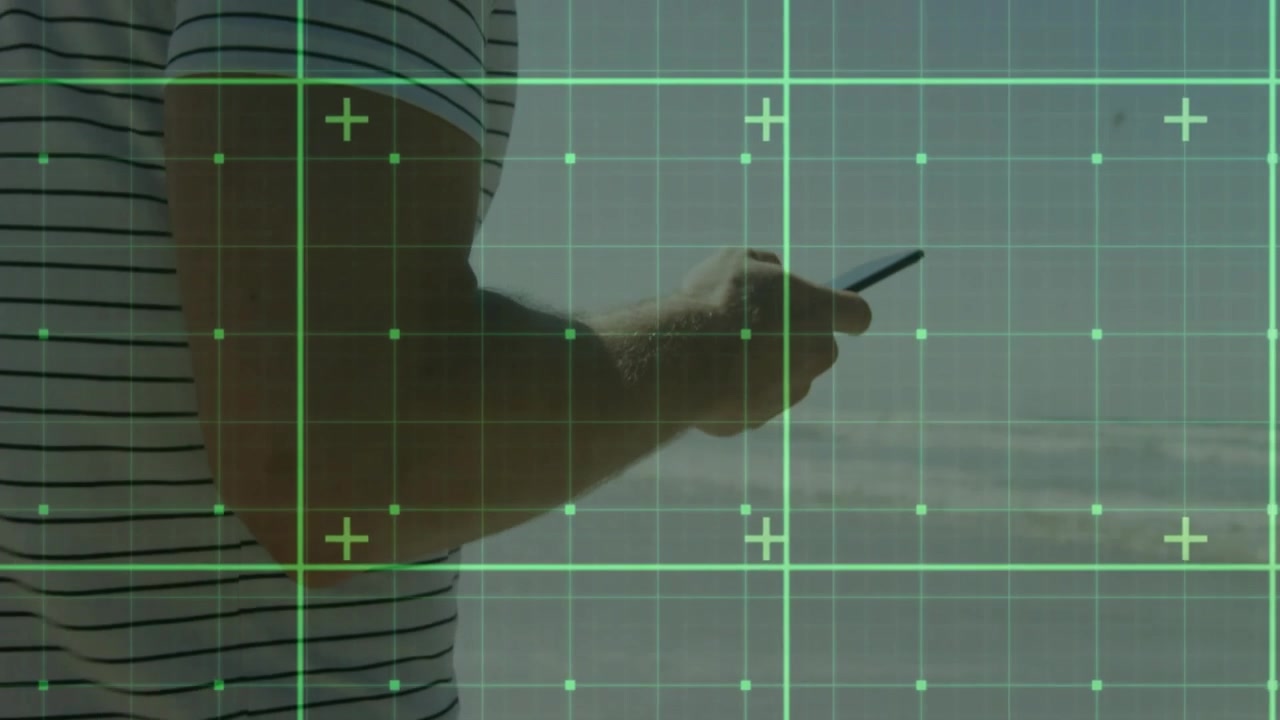 Camera panning upward, man standing on shoreline, tapping smartphone with green tech grid scanning