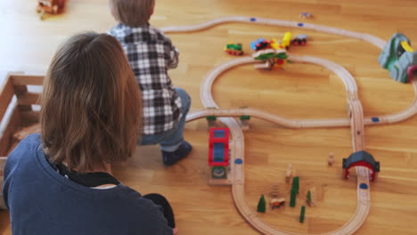 young boy standing up from his mothers lap to move a toy train