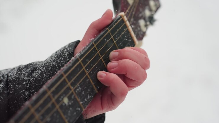 крупный план руки, играющей на гитаре на покрытых снегом струнах, создавая идеальную гармонию между музыкой и спокойной красотой зимы, с холодными текстурами на черном рукаве и шее гитары