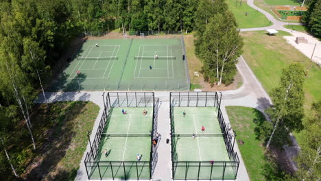 aerial tilting down on four green outdoor paddle tennis courts filled with athletic fitness sports people training and playing racket sports at golf resort near sea side at summer tennis paddle camp