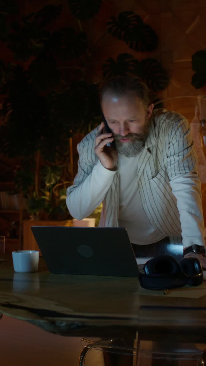 Man working late at night on laptop while talking on phone