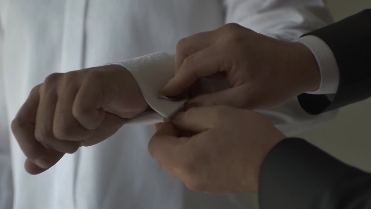 Man Helping Groom By Buttoning The Cuff Of White Sleeve. - close up