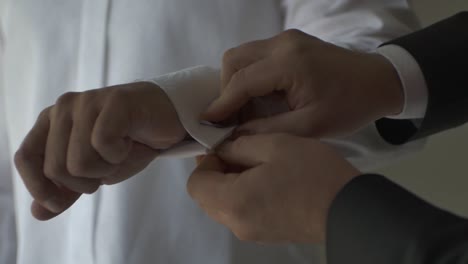 man helping groom by buttoning the cuff of white sleeve. - close up