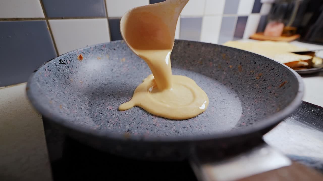 Slow motion shot of thick golden pancake batter being poured in warm kitchen pan