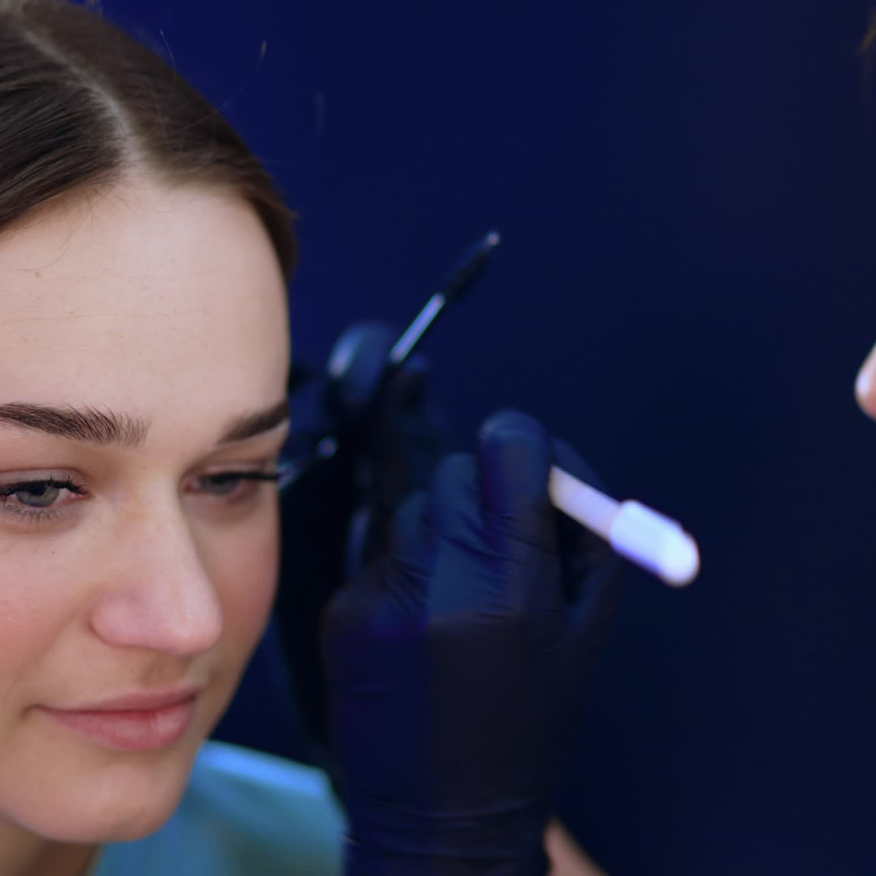 Young beautiful girl in a beauty salon. Beautician draws white lines around client's eyebrows to mark their limits for future procedure. Close up